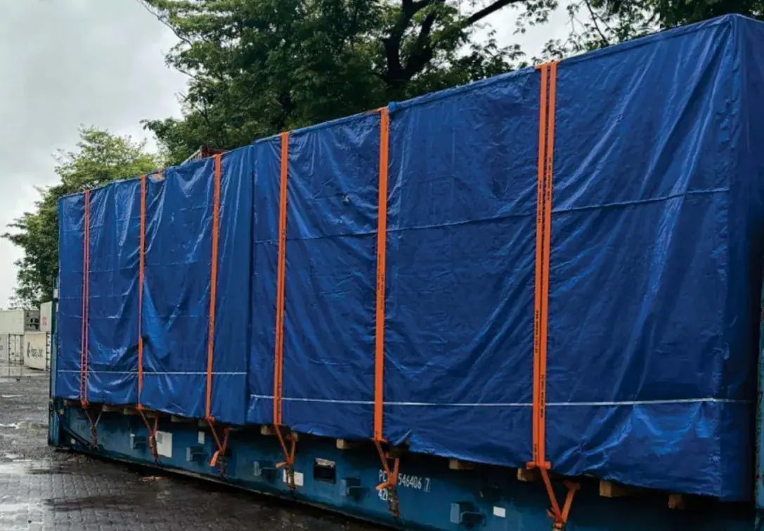 Cargo under a blue tarpaulin secured with orange straps on a flat rack