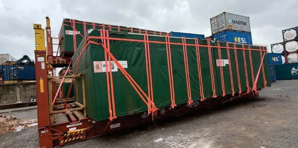 Green tarpaulin load lashed with orange straps on a flat rack at the terminal