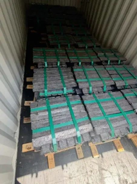 Metal ingots on pallets, strapped with green bands inside a container