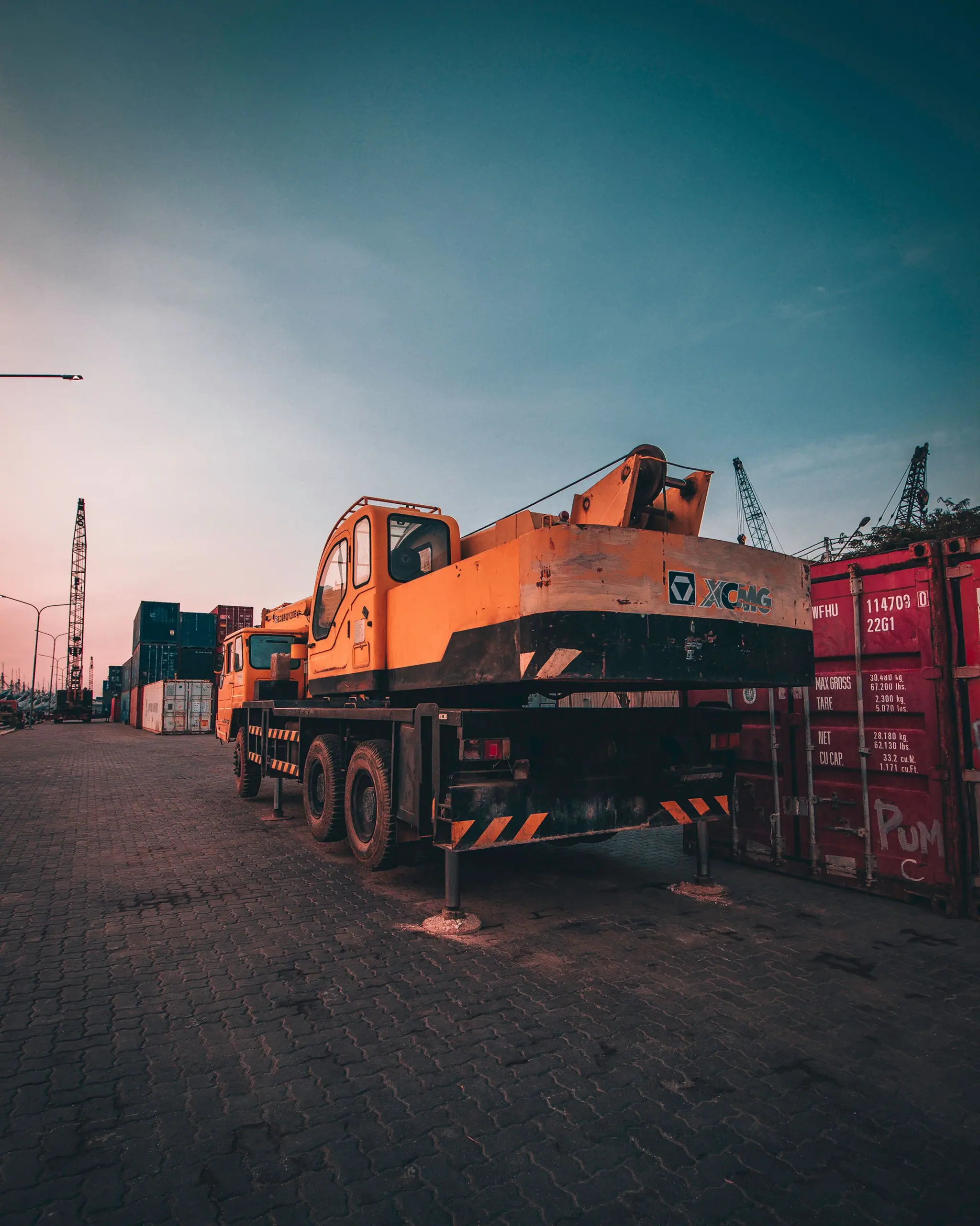 Orange mobile crane parked beside stacked containers in a port yard
