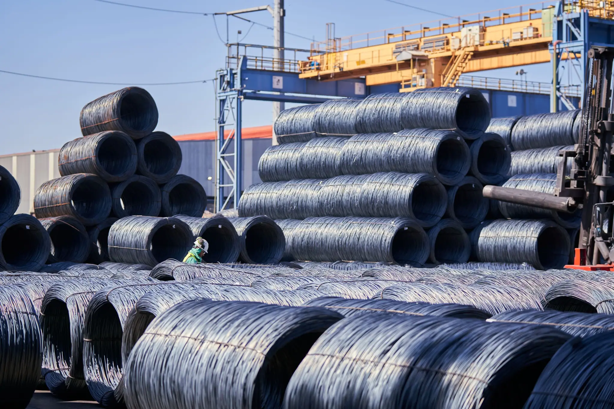 Rows of steel wire coils stacked in a port yard beneath a gantry crane